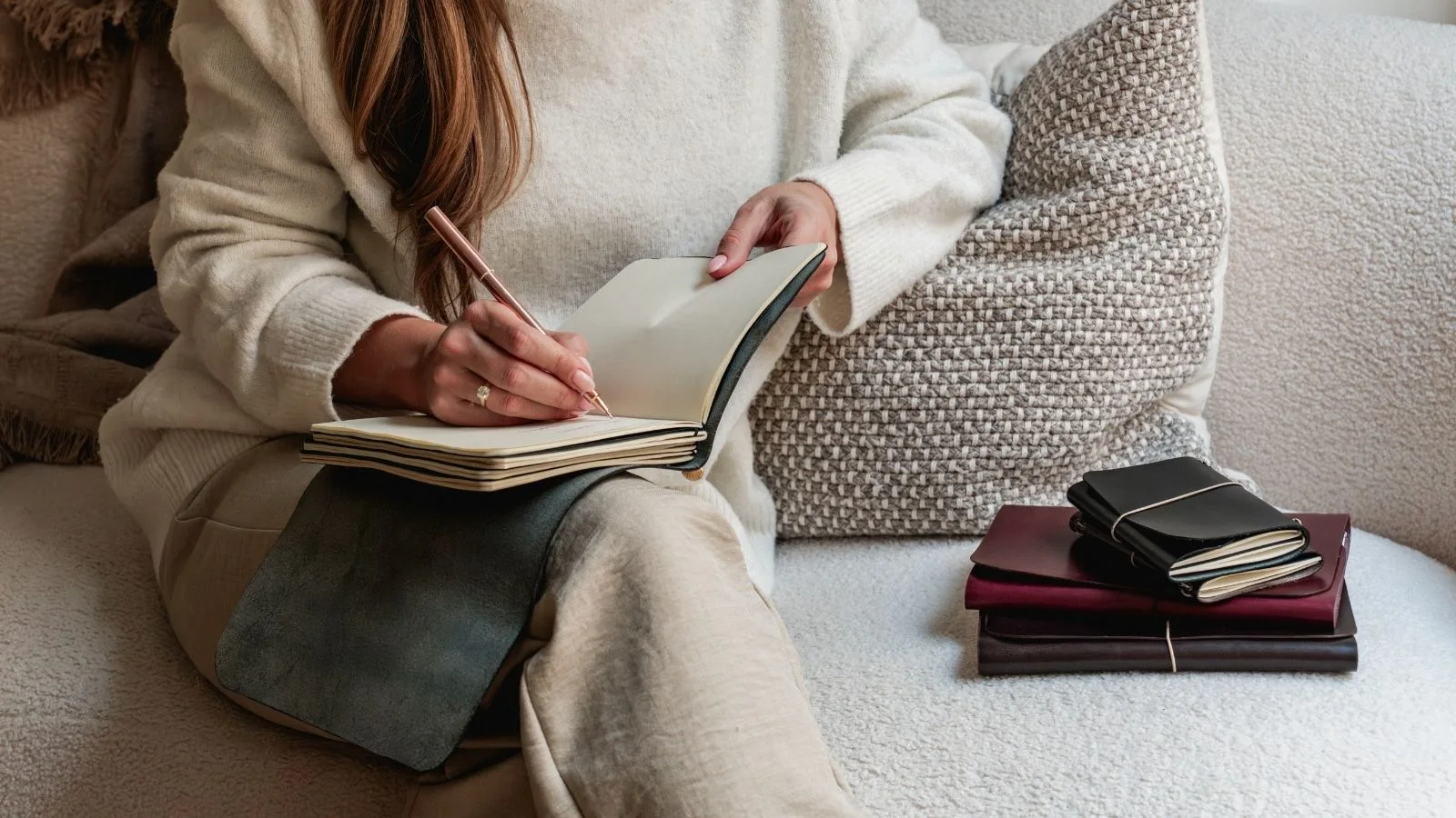 Una persona escribiendo en un journal notāre en el sofá, con Muse y Nomad apilados a un lado.