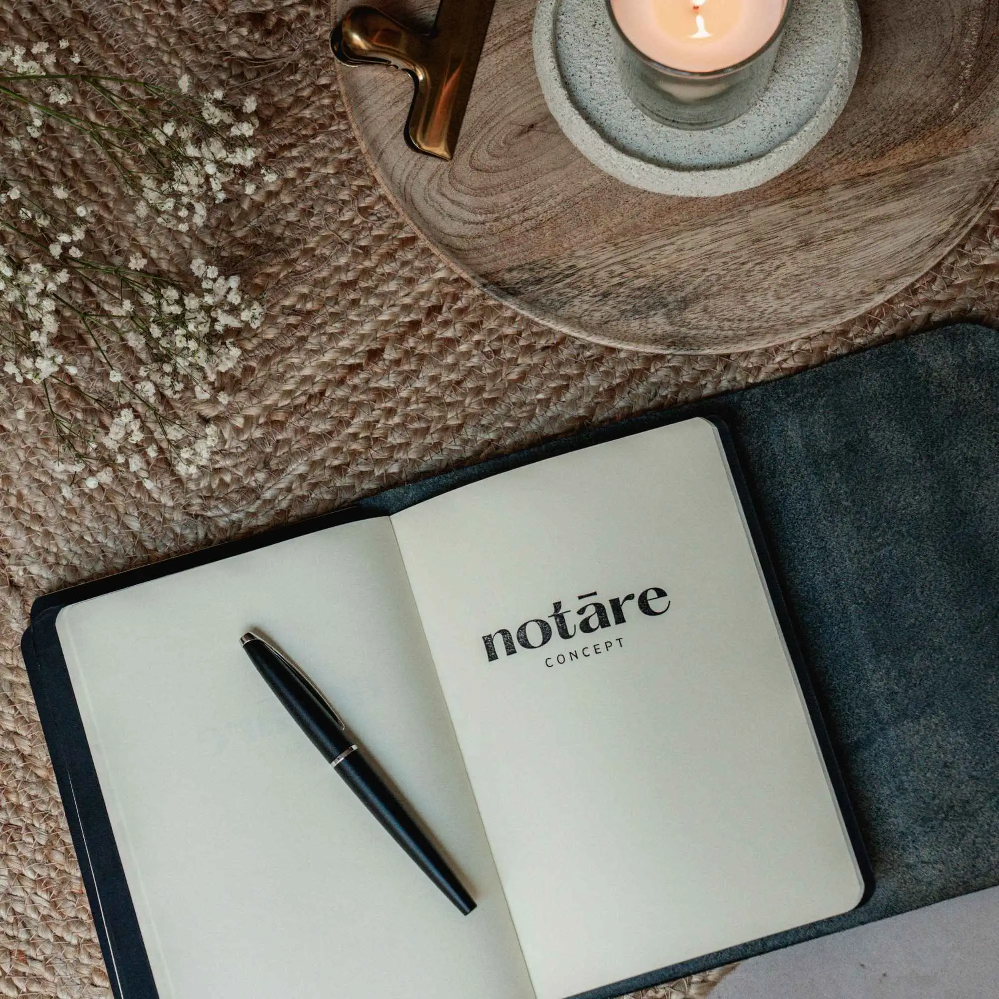 Journal notāre abierto sobre una alfombra, con bolígrafo y una vela encendida en una bandeja de madera.