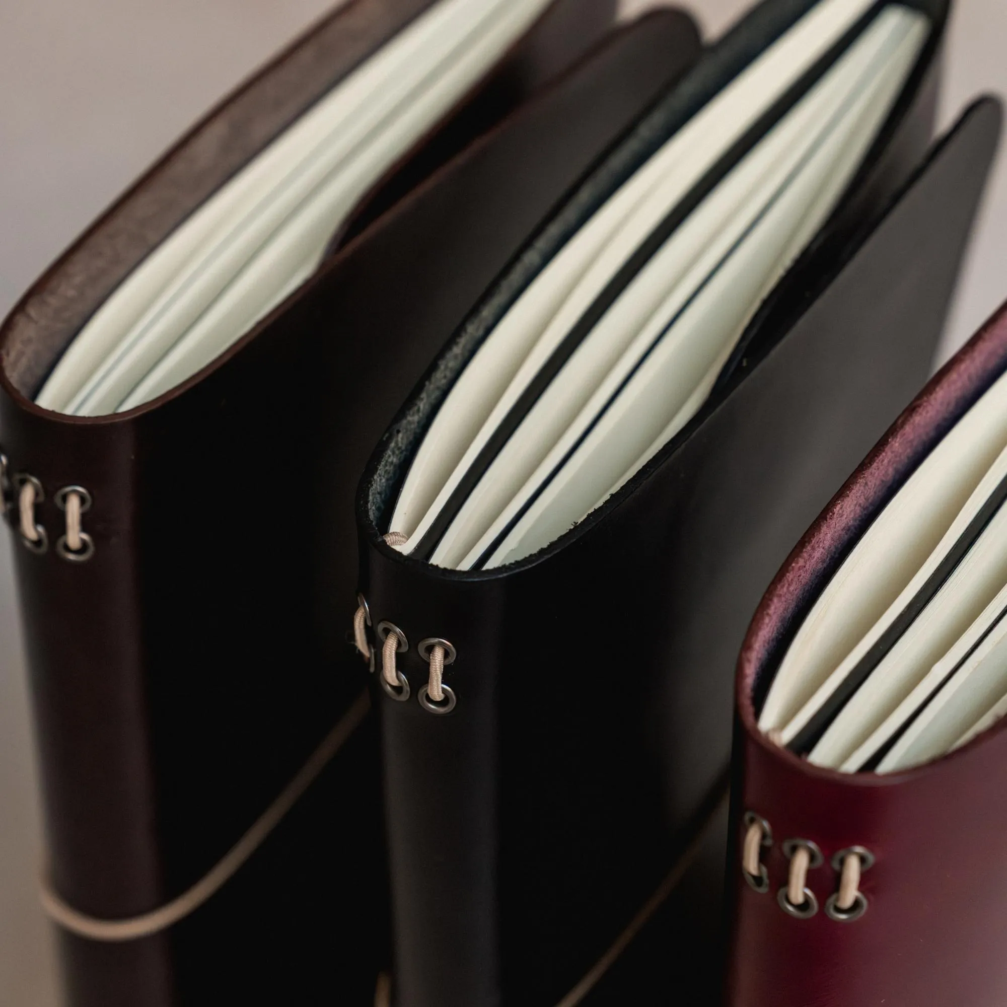 Detalle del canto y las páginas de varios journals notāre de cuero, con ojales metálicos y elásticos.