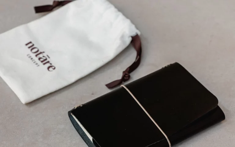 Muse noir de notāre cerrado con elástico, junto a su bolsa de viaje de algodón con logo notāre.